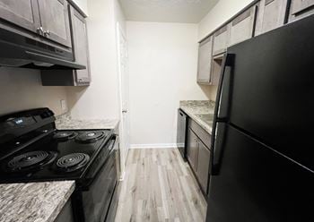 An empty kitchen with black appliances and wood flooring
